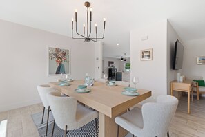 Ein zeitgemäßes Esszimmer mit einem Holztisch, gedeckt für vier Personen, weißen Stühlen und einer Chandelüster.