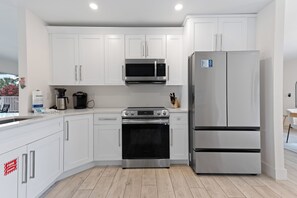 A modern kitchen with white cabinetry, stainless steel appliances, and a wooden floor. - 💮Private Pool Home-Canal Front-Pet Friendly-3BR The Pink Lily💮 (Fort Myers)