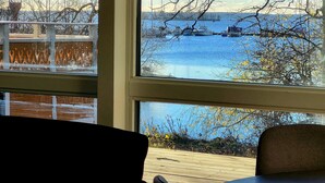 A view from inside a room with a large window overlooking a wooden deck and a body of water with boats.