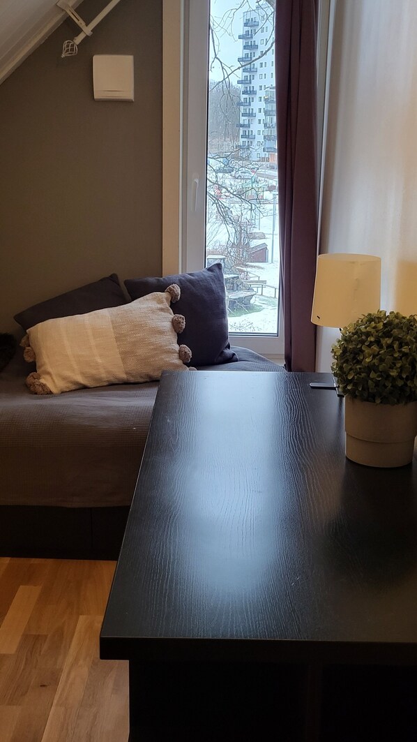 A modern living room with a sofa, a dark wooden table, a potted plant, and a view of a building through a window.