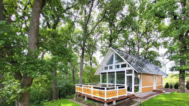 A modern house with a large glass front, wooden deck, and surrounded by lush greenery.