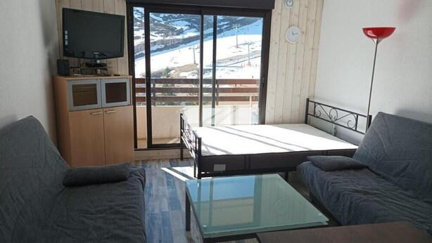 Un salon avec un canapé, une table basse en verre, un téléviseur posé sur un meuble en bois et un balcon offrant une vue sur un paysage enneigé.