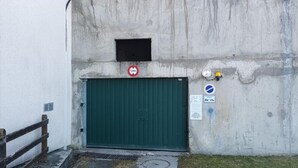 Un bâtiment en béton avec une porte verte, un panneau indiquant qu’il est interdit de se garer et un panneau bleu signalant une zone de chargement et de déchargement.