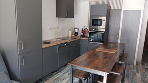 Une cuisine moderne avec des meubles gris, un plan de travail en bois, un four encastré et une table à manger avec des bancs.