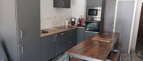 A modern kitchen with grey cabinets, a wooden countertop, a built-in oven, and a dining table with benches.