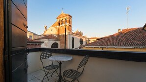 Un balcon avec deux chaises et une petite table, d’où l’on peut admirer un bâtiment historique doté d’un clocher.