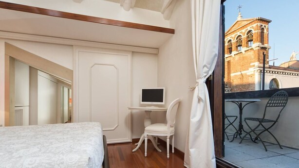 Une chambre d’hôtel avec un lit, un bureau équipé d’un ordinateur, une chaise et une vue sur un bâtiment doté d’un clocher.