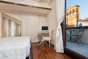 Een hotelkamer met een bed, een bureau met een computer, een stoel en uitzicht op een gebouw met een klokkentoren.