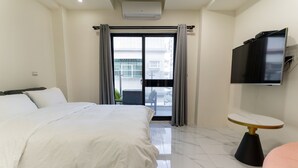 A hotel room with a large bed, a flat-screen TV mounted on the wall, a small round table, and a balcony with a view of the outside. - Yan Yingchenxi (Kaohsiung)