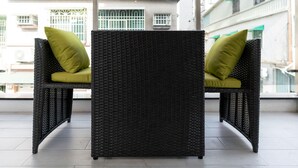 A wicker chair with a cushion, positioned on a balcony with a view of buildings. - Yan Yingchenxi (Kaohsiung)