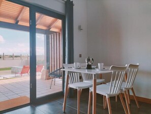A dining area with a table and chairs, a coffee machine, and a view through a glass door to an outdoor patio with chairs. - Apartamentos Walden by gaiarooms (Morille)