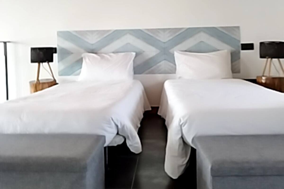 Une chambre d’hôtel moderne avec deux lits simples, une tête de lit à motifs géométriques et un plafond en bois.