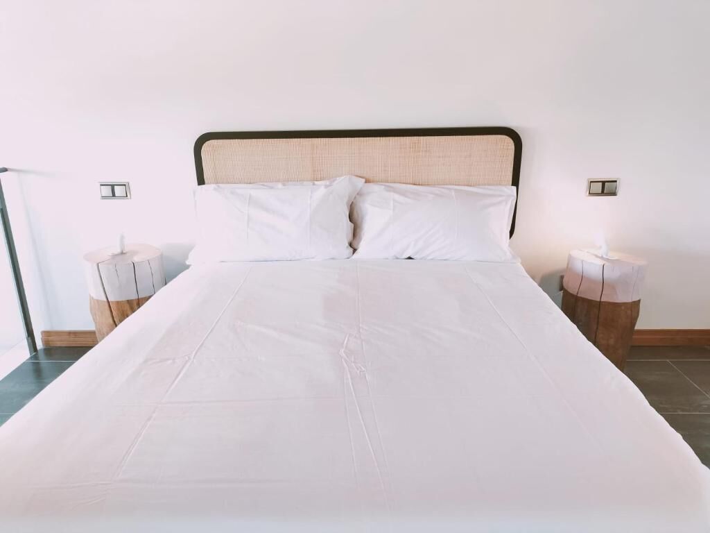 A neatly made bed with white linens, two bedside tables with lamps, and a plain wall.