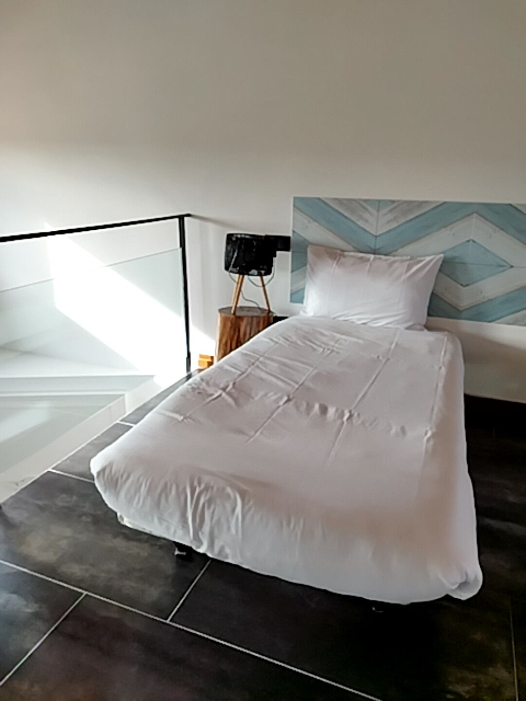 Quarto moderno com uma cama grande, mesa de cabeceira e luminária fixada na parede.
