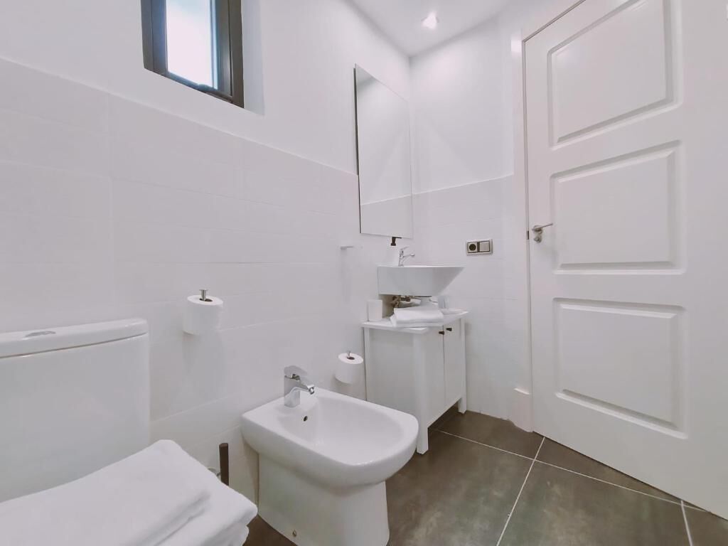 A modern bathroom with a toilet, bidet, sink, and mirror.