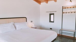 Een slaapkamer met een groot bed, een nachtkastje, een hanglamp, een raam en een bankje.