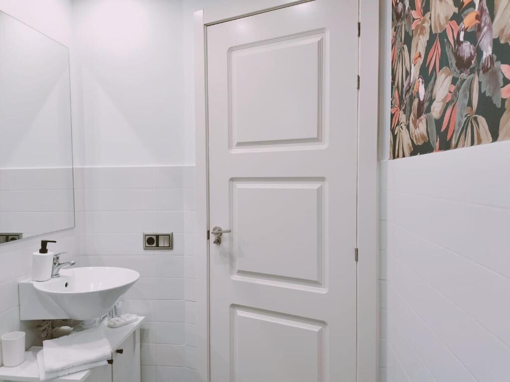 Une salle de bain avec un lavabo blanc, un miroir et une porte ornée d’une fresque florale sur le mur.