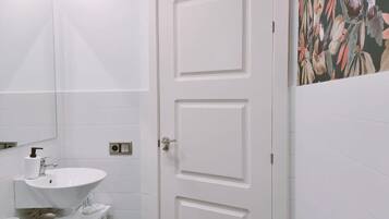 Une salle de bain avec un lavabo blanc, un miroir et une porte ornée d’une fresque florale sur le mur.
