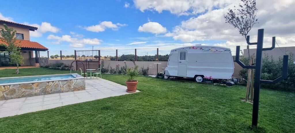 A backyard with a swimming pool, a white RV, and a cactus.