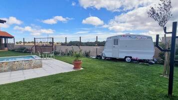 A backyard with a swimming pool, a white RV, and a cactus.