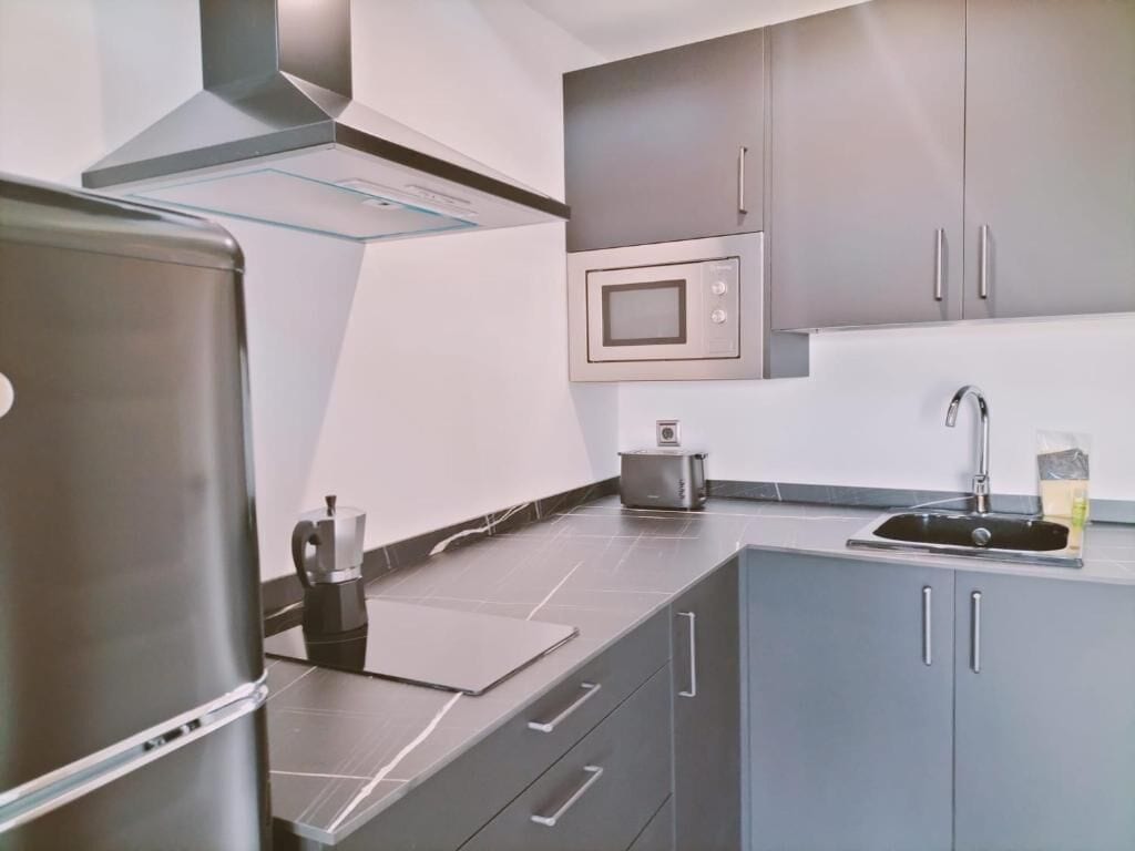 A modern kitchen with stainless steel appliances, grey cabinets, and a built-in microwave.