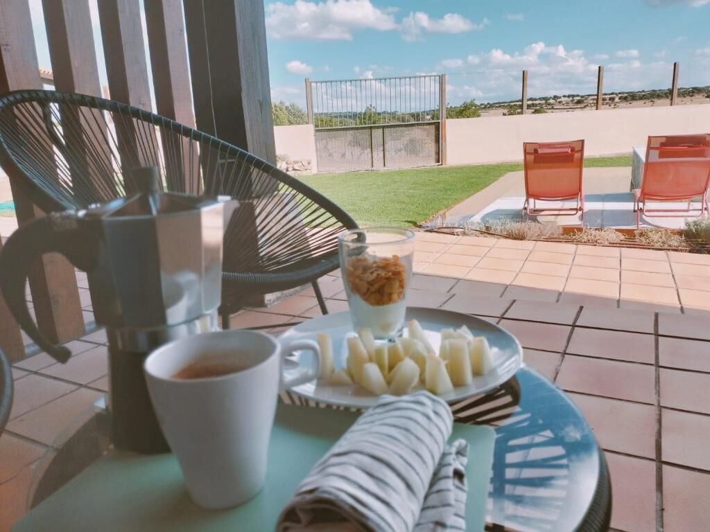 A patio with a table set for breakfast, including a cup of coffee, a plate of sliced fruit, and a rolled-up napkin.