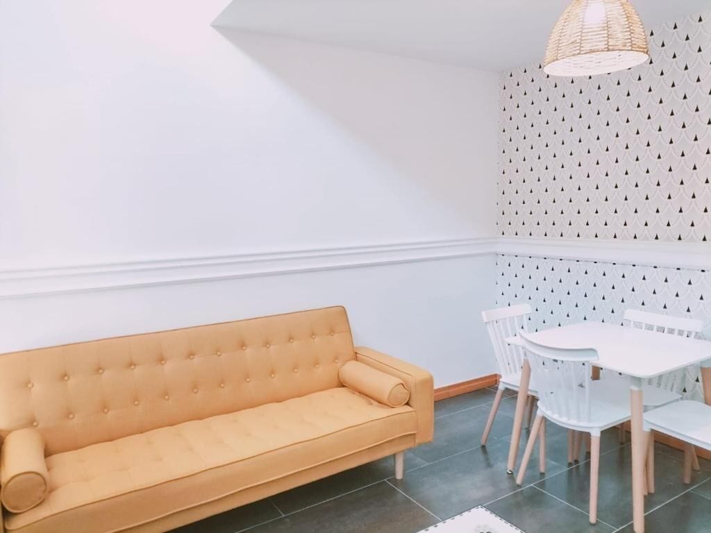 Une pièce avec un canapé jaune, des chaises blanches et une petite table.