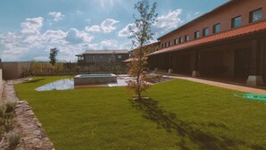 Een verzorgd gazon met een kleine vijver, een heldere lucht en een modern gebouw met veel ramen.
