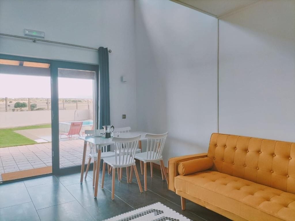 A modern interior with a sofa, a table with chairs, and a view through a glass door.