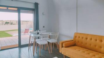 A modern interior with a sofa, a table with chairs, and a view through a glass door.