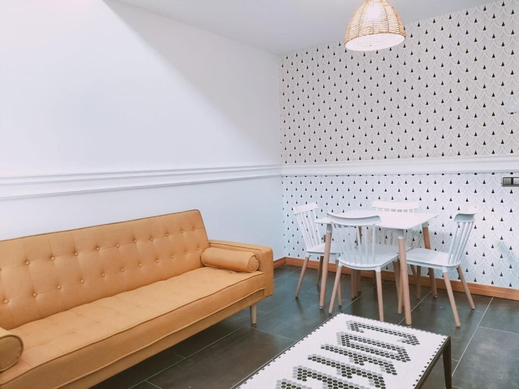 Una habitación con un sofá, una mesa redonda con sillas y una alfombra estampada.