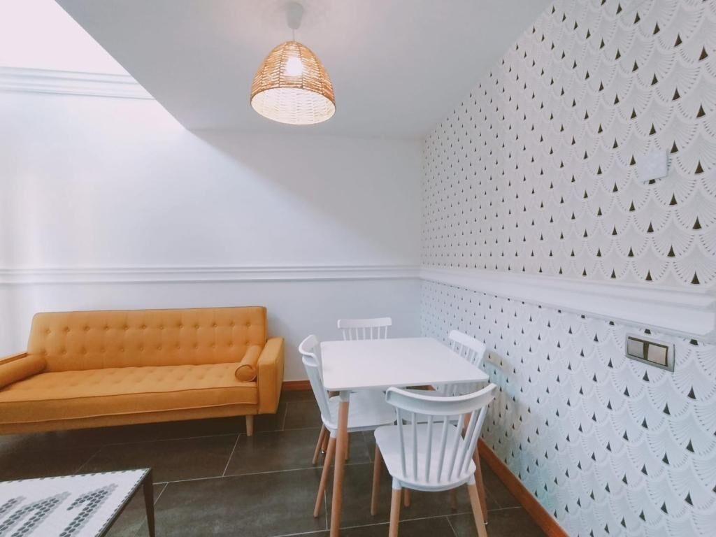 A room with a white sofa, a white dining table with chairs, a woven pendant light, and a patterned wall.