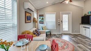 A dining area with a wooden table, chairs, and a decorative rug. There is a sofa with cushions and a television in the background. - Vilonia Country Cabin w/ Grill, Fire Pit + More! (Vilonia)