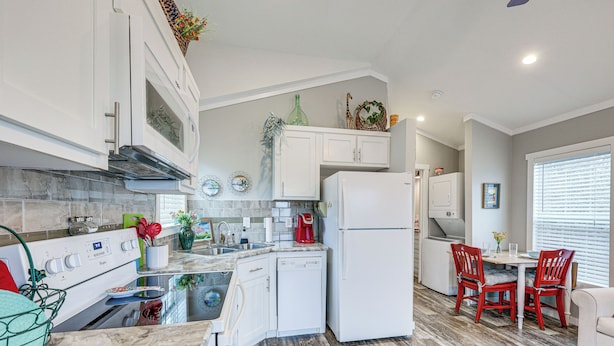 A modern kitchen with white cabinets, a built-in oven, and a dishwasher. There is a dining area with a table and chairs, and a window with blinds. - Vilonia Country Cabin w/ Grill, Fire Pit + More! (Vilonia)