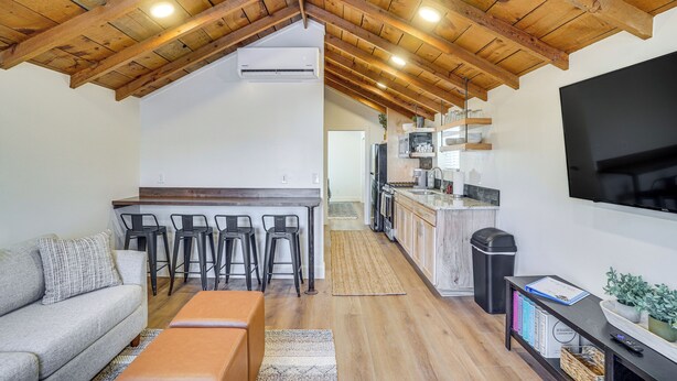 Een moderne keuken met een houten plafond, een eethoek met barkrukken, een bank en een aan de muur bevestigde televisie.
