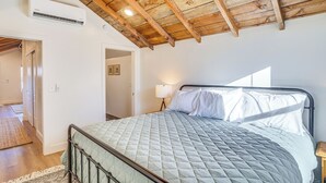 Een slaapkamer met een bed, houten balken in het plafond, een wandairconditioner en een bedlampje.