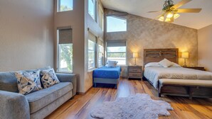 Ein Schlafzimmer mit zwei Betten, einem Schlafsofa, einem Deckenventilator und großen Fenstern.