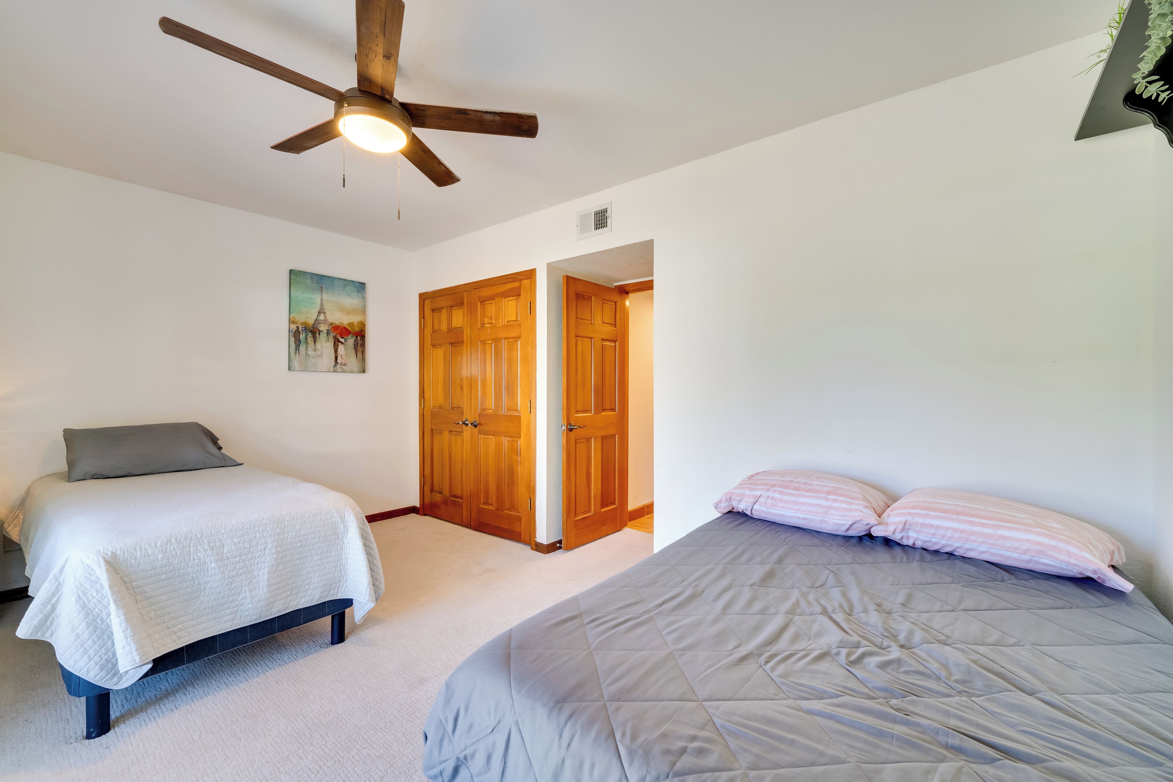 A bedroom with two beds, a ceiling fan, and wooden doors.