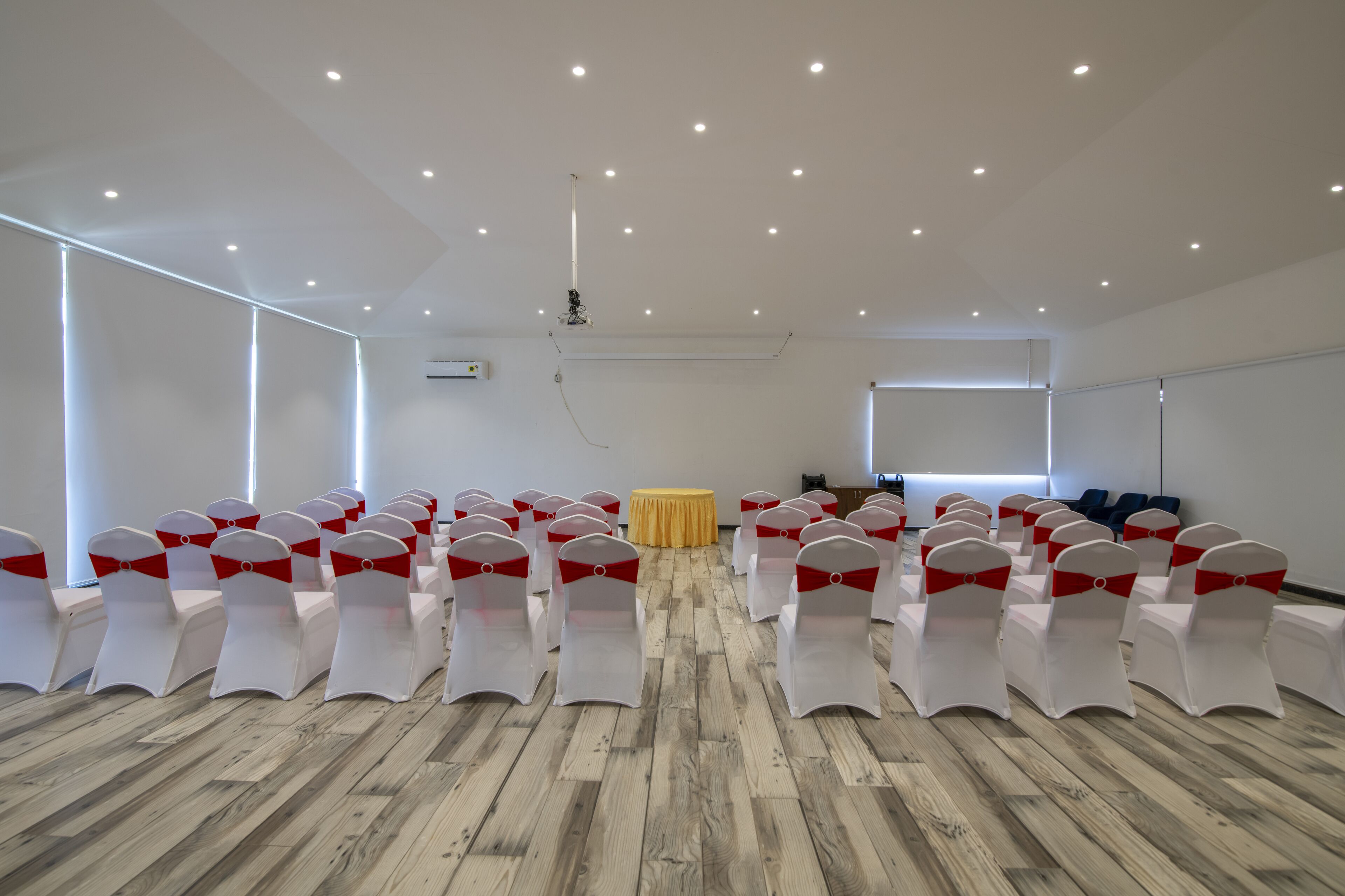 A conference room with rows of white chairs with red sashes, a projector, and a table with a yellow cloth.