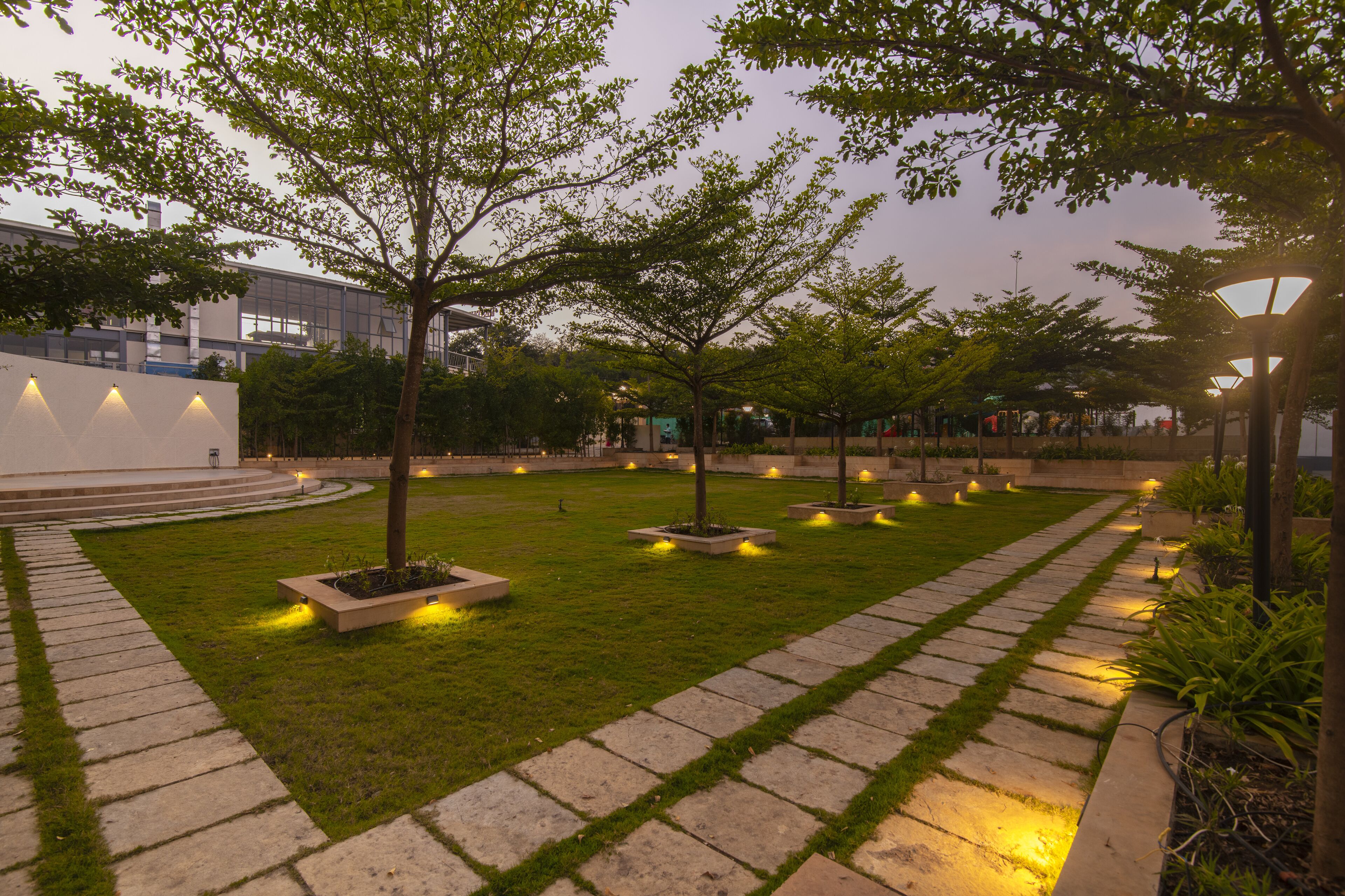 Un jardín ajardinado con un sendero empedrado, árboles y luces iluminadas.