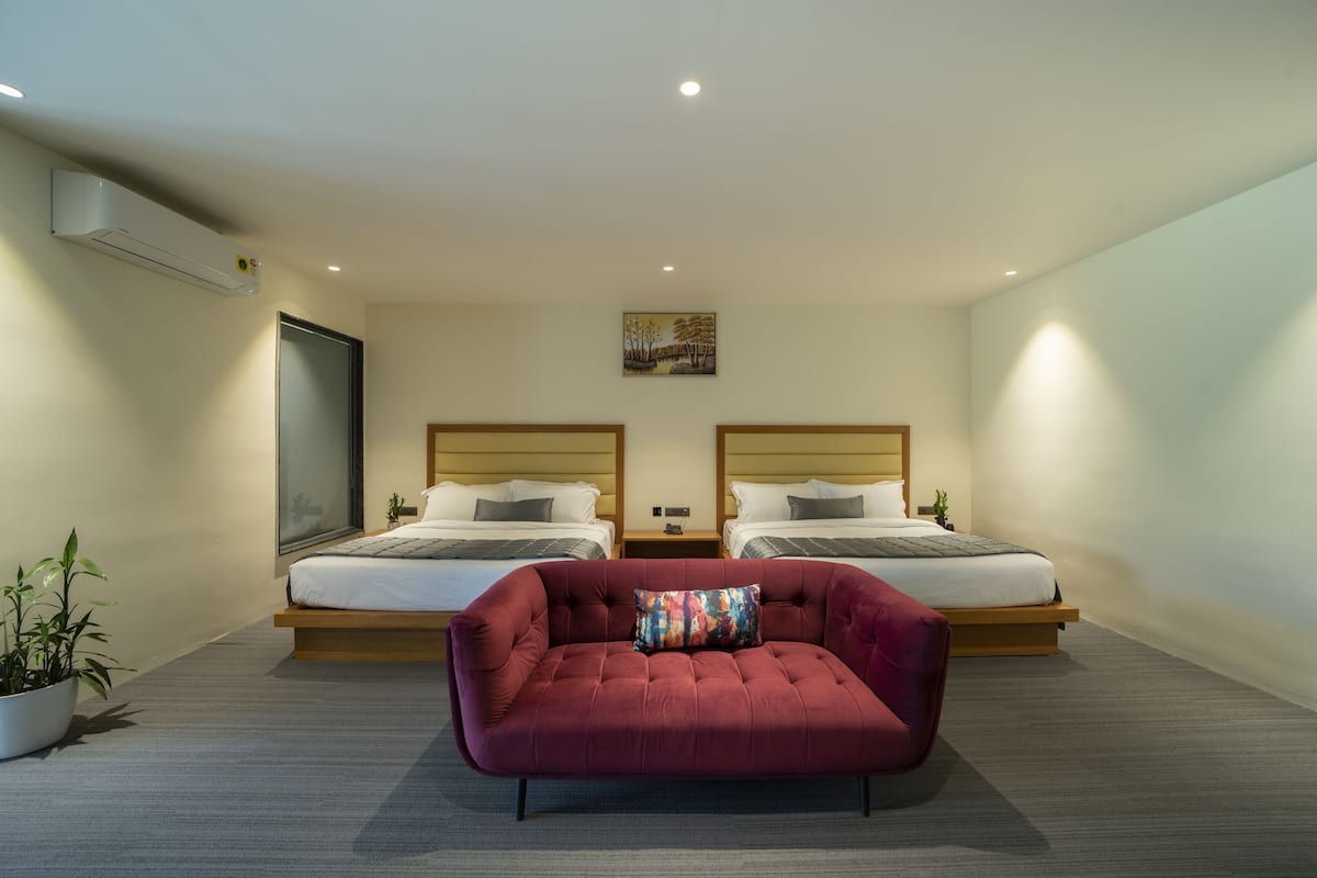 Una habitación de hotel moderna con dos camas, un sofá rojo y una planta en maceta.
