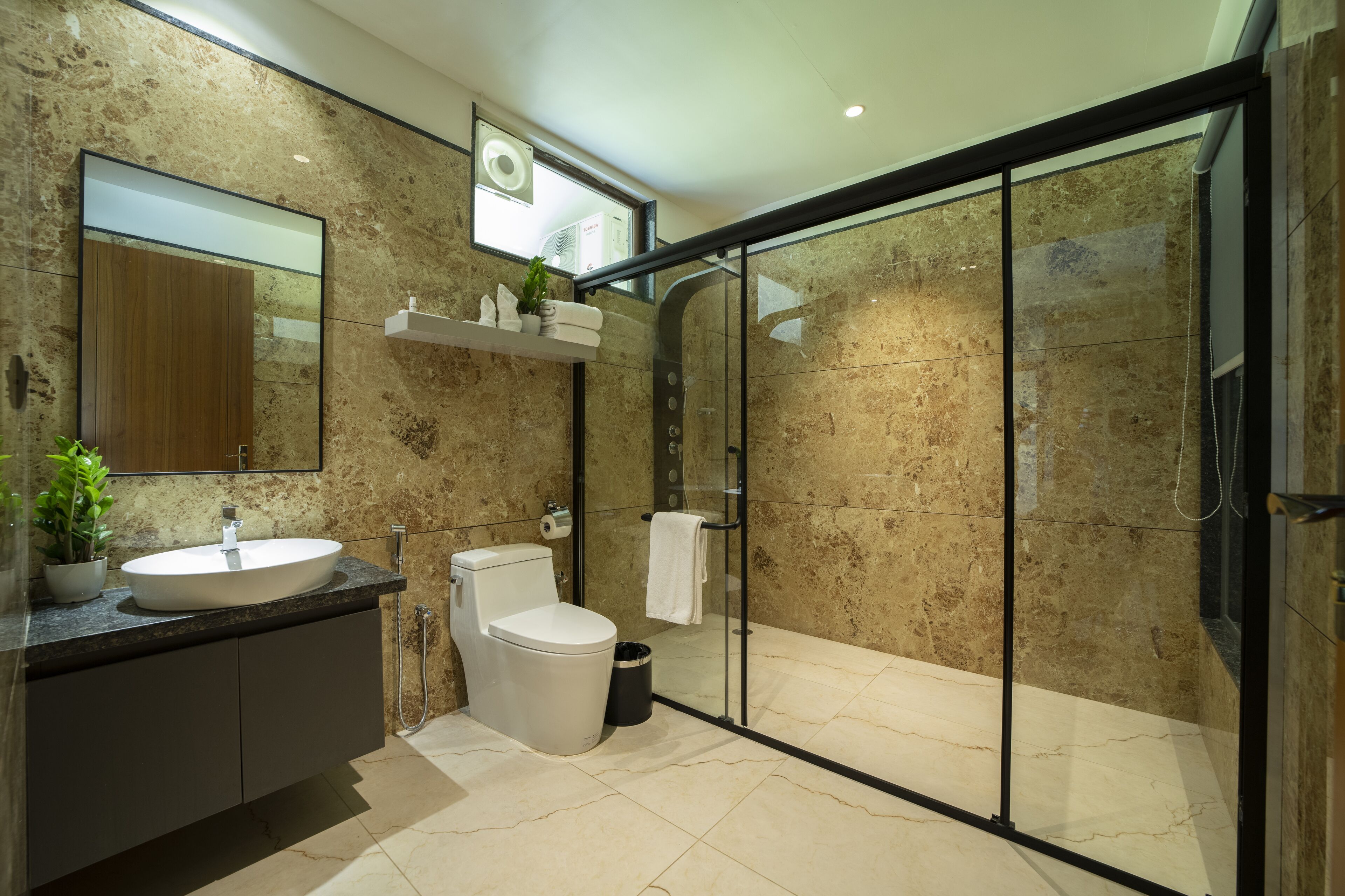 A modern bathroom with a marble sink, toilet, and a glass-enclosed shower.