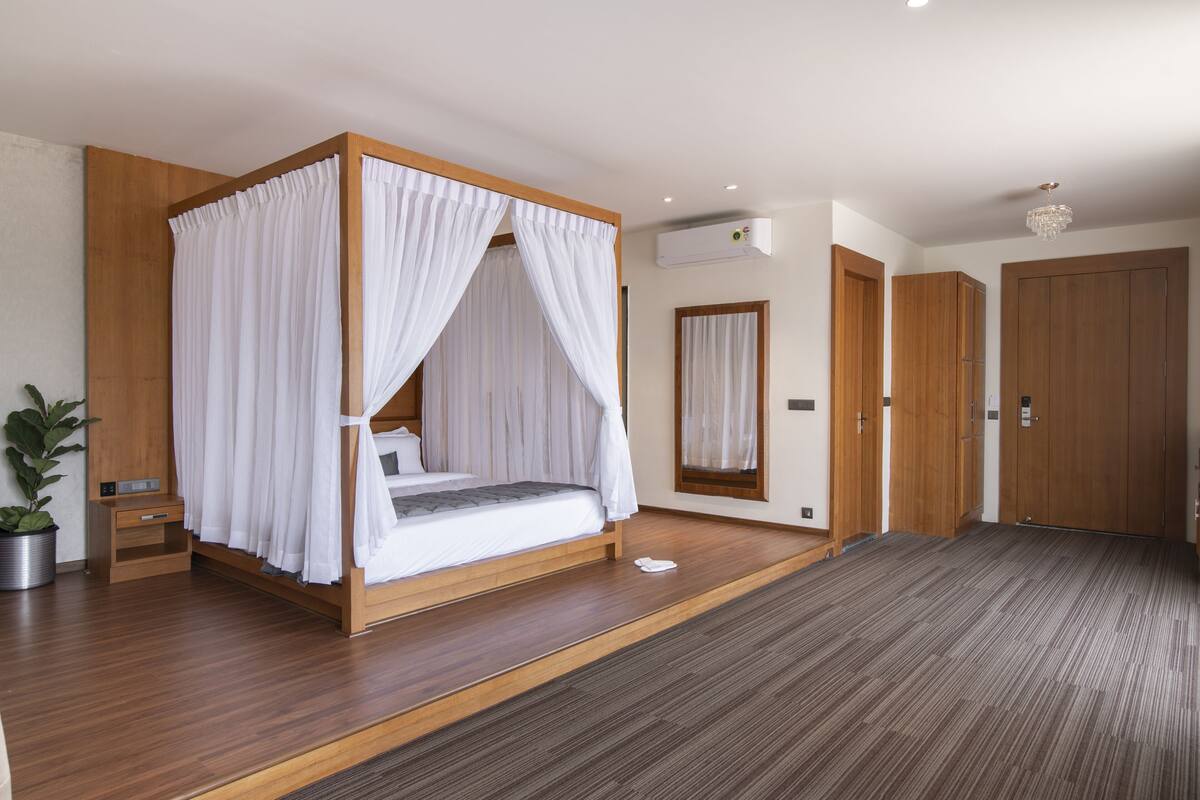 Un dormitorio con cama con dosel, suelo de madera, una planta en maceta y un espejo grande.