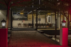 Un área de comedor al aire libre con mesas y sillas, un paseo techado y un edificio al fondo.