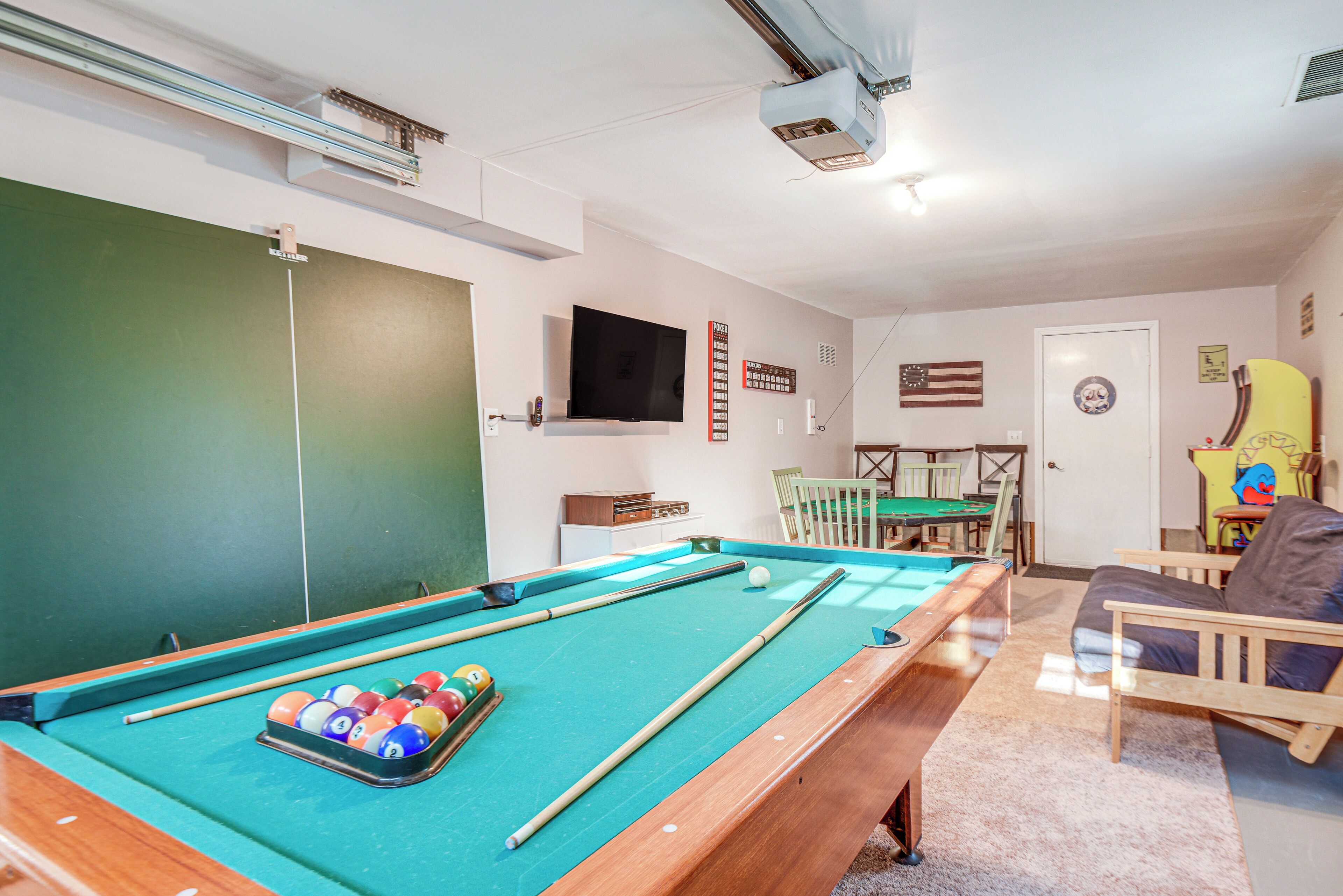 A pool table with balls, a television mounted on the wall, and a door with a circular emblem.