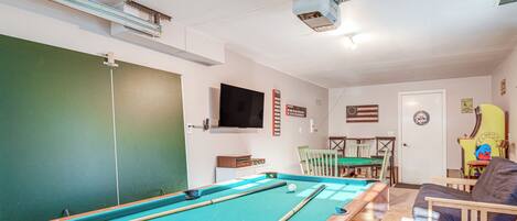 A pool table with balls, a television mounted on the wall, and a door with a circular emblem.