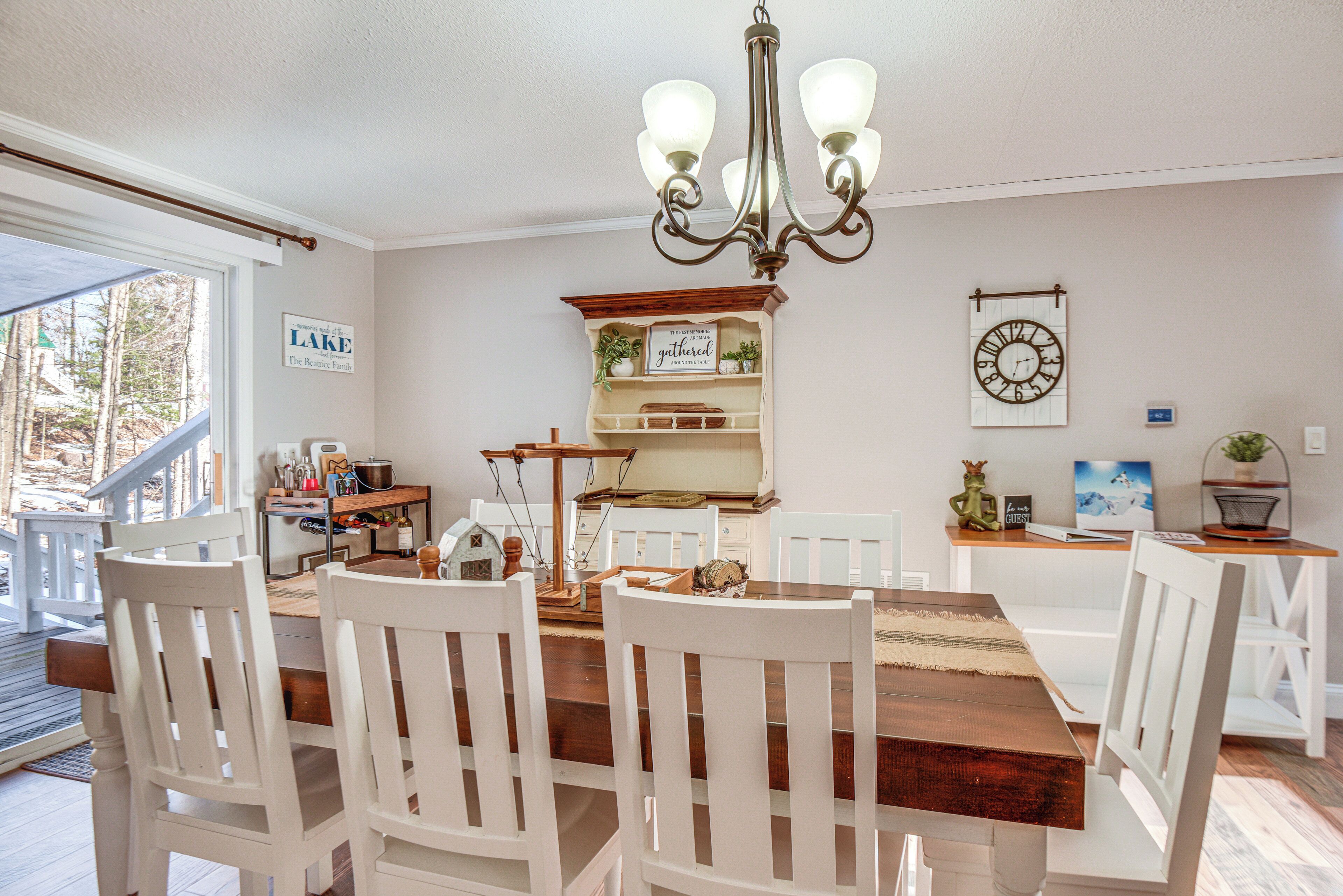 Een eetruimte met een houten tafel en witte stoelen, een kroonluchter, een klok en een bord met de tekst 'The Belleville Family'.