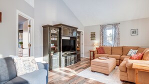 Una sala de estar con un sofá azul, un sofá beige, un mueble de entretenimiento de madera y un televisor.