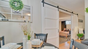 A dining area with a table set for four, a sliding barn door, and a view into a living room with a sofa and a plant. - Cozy Lakeview Retreat, Close to Bull Shoals Lake! (Lakeview)