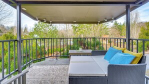 A covered outdoor seating area with a sofa and table, surrounded by a metal railing, overlooking a garden with trees and a pathway. - Sauna, Pickleball Court & Game Room: Sultan Villa! (Sultan)